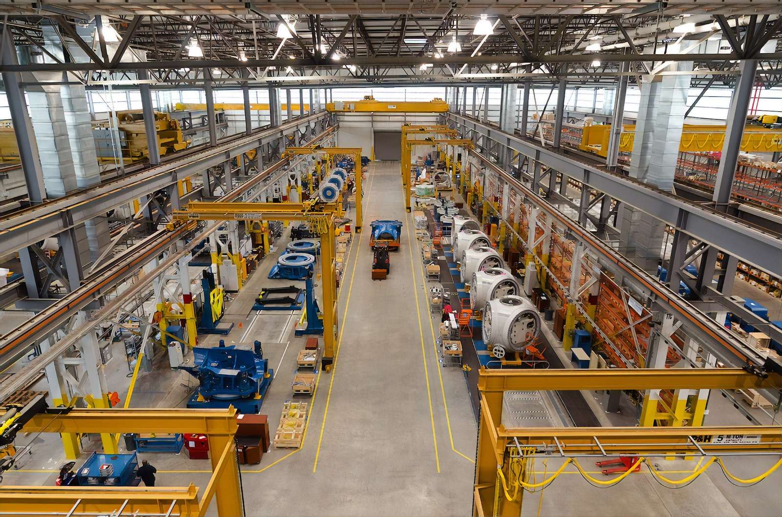 Manufacturing plant floor with overhead cranes and machinery along the production lines
