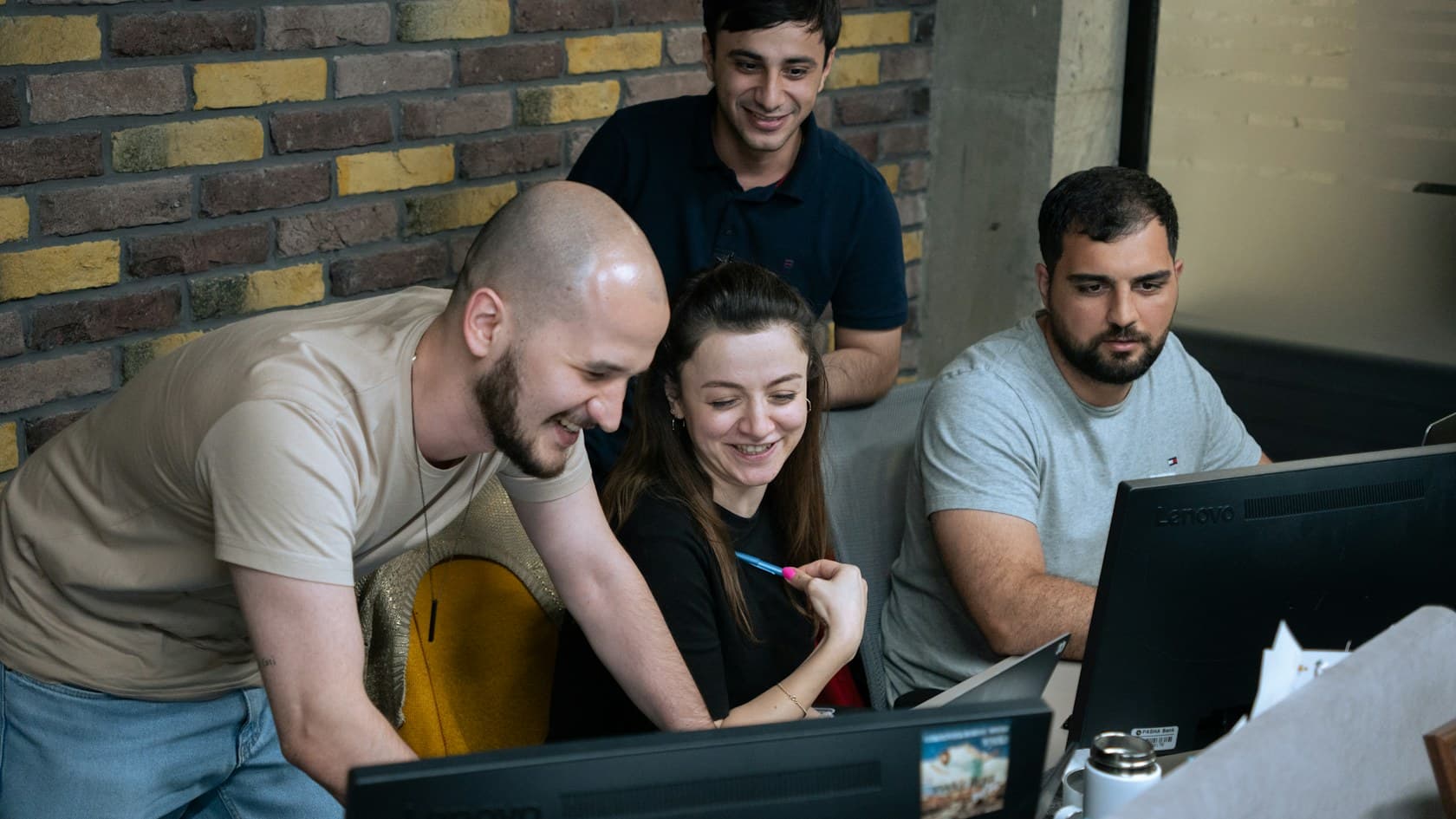 Four colleagues smiling as they review something together on an office monitor