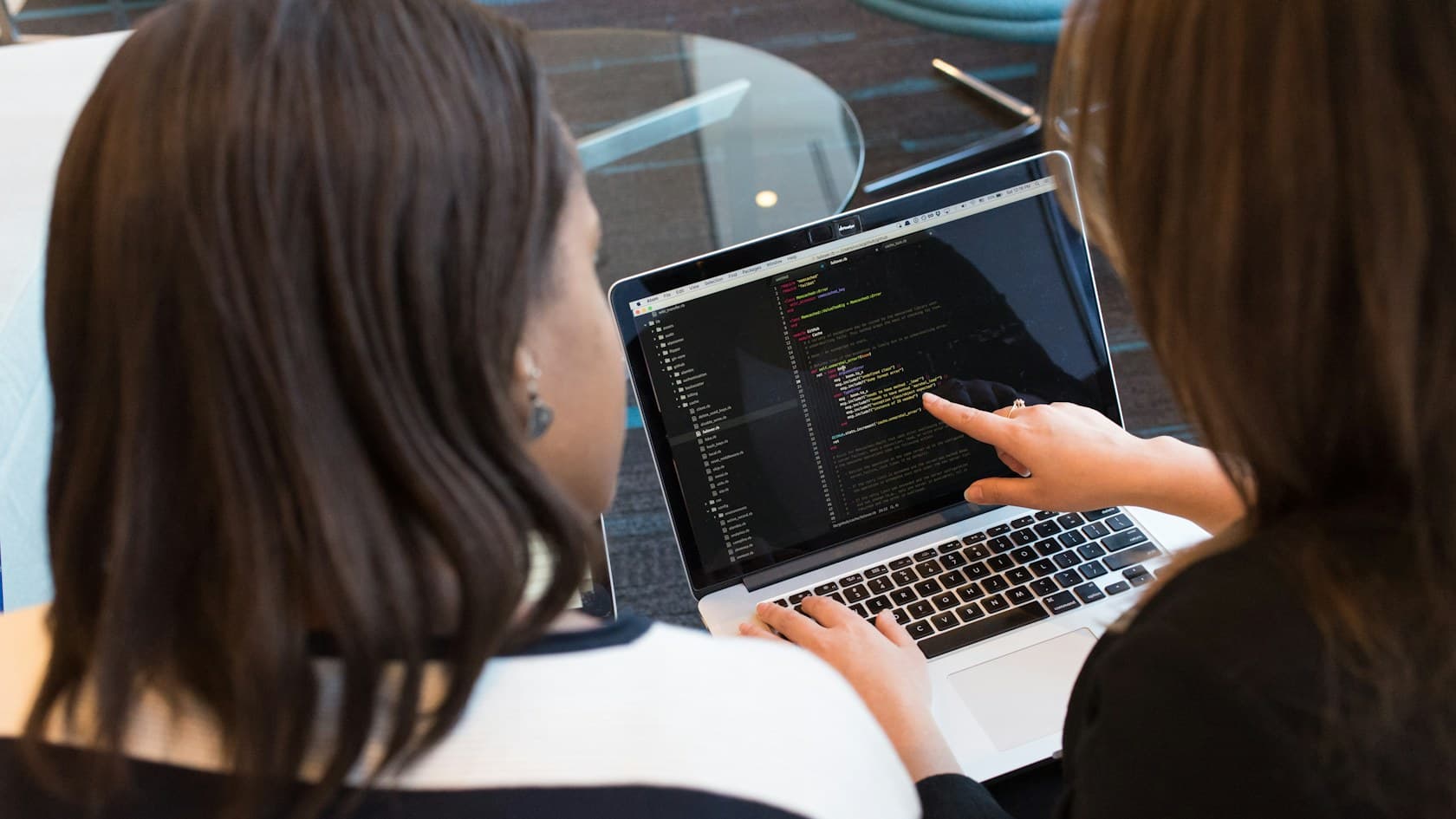 Two colleagues pointing at lines of code on a laptop to review them together