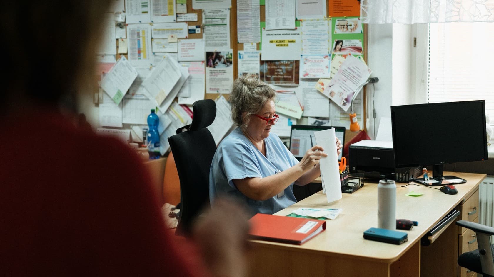 Nurse in scrubs reviewing paperwork at her desk in a care home office