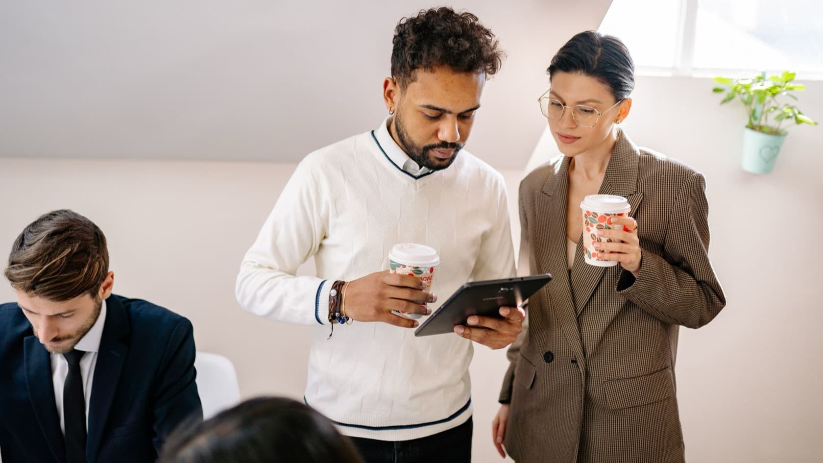 Colleagues with morning coffee reading updates on a tablet in a bright office