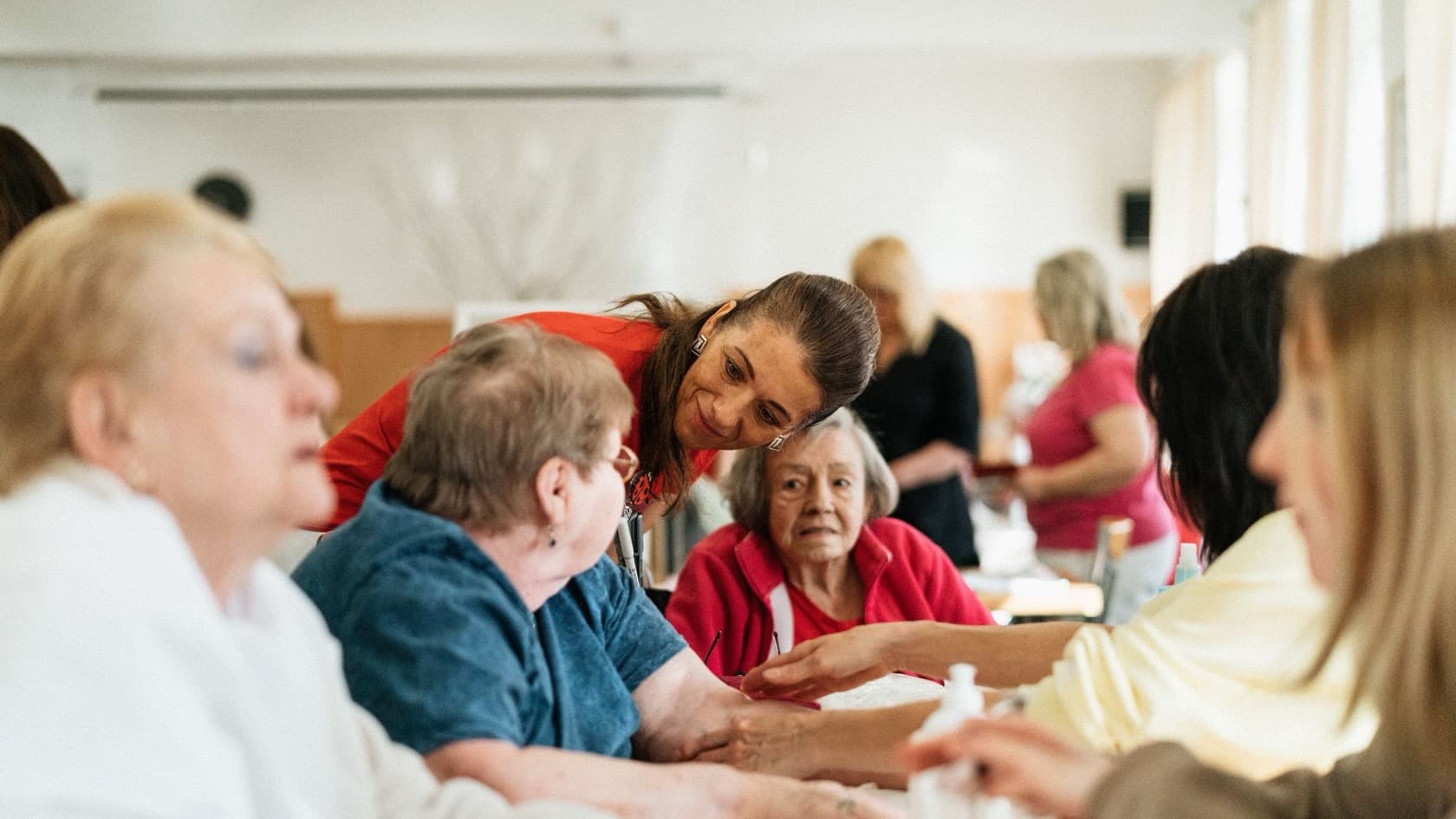 Carer in red leaning in to help residents during a table activity session
