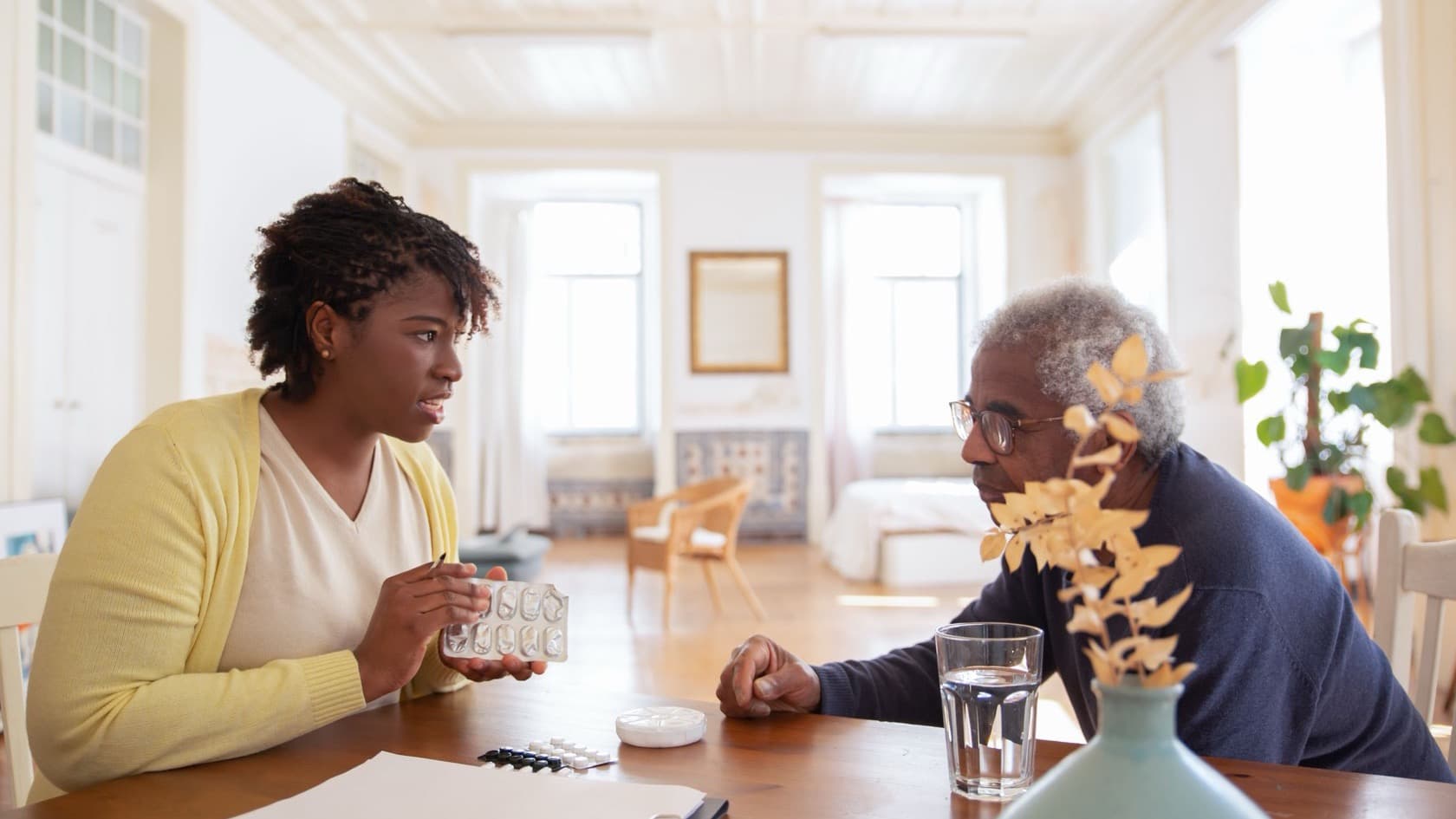 Carer going over medication with an older resident at a table, notes folder in front of them
