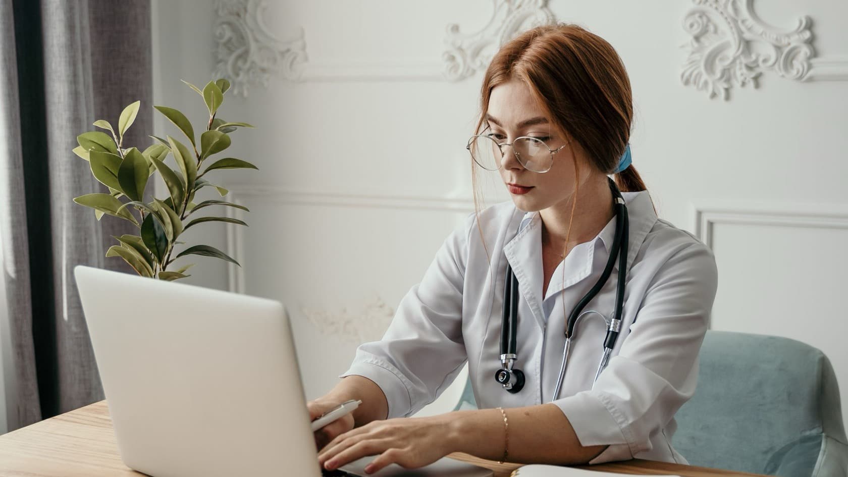 Nurse manager typing on a laptop at a wooden desk in a bright, homely office