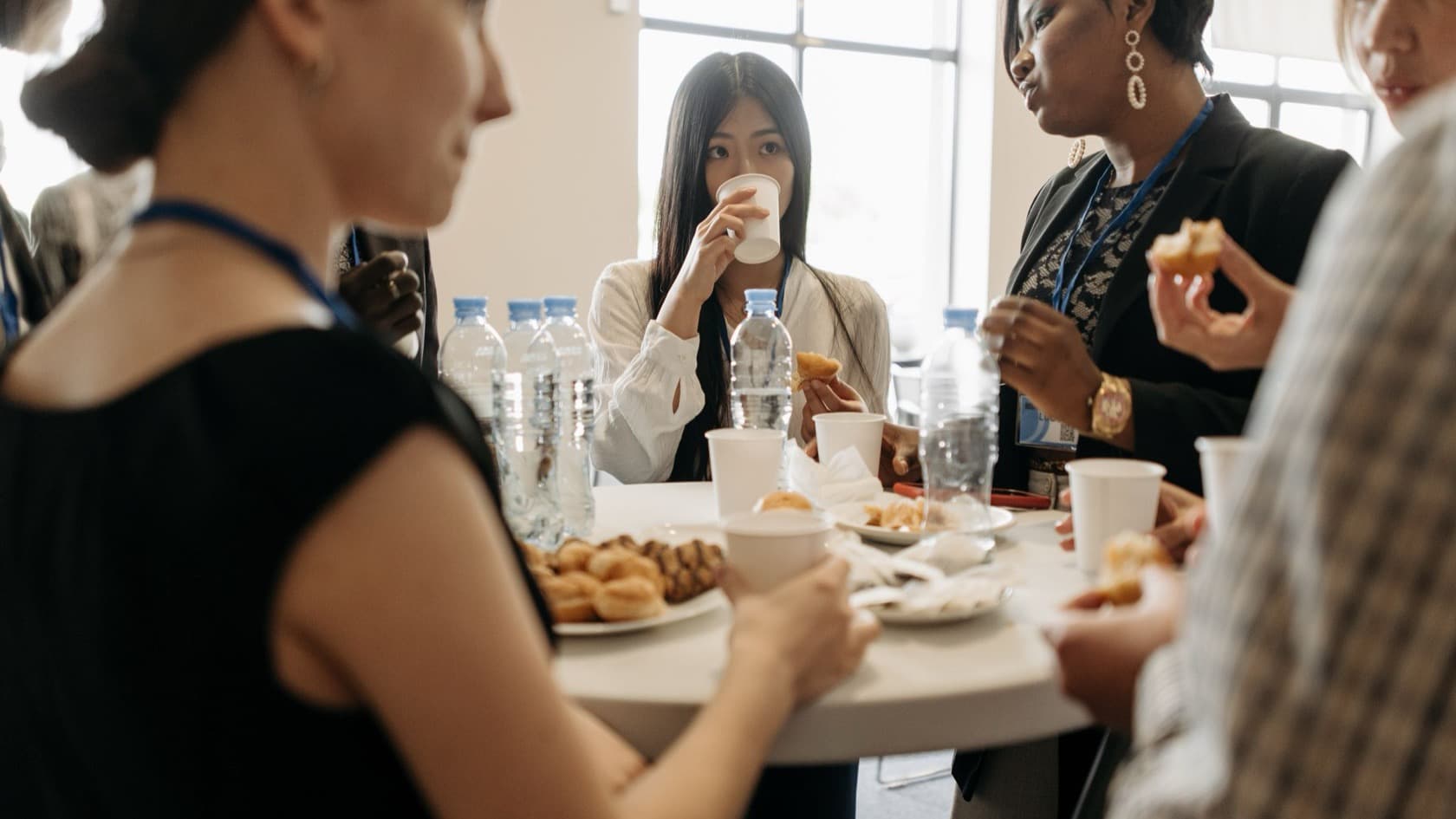 Professionals with lanyards talking over coffee and pastries at a networking table
