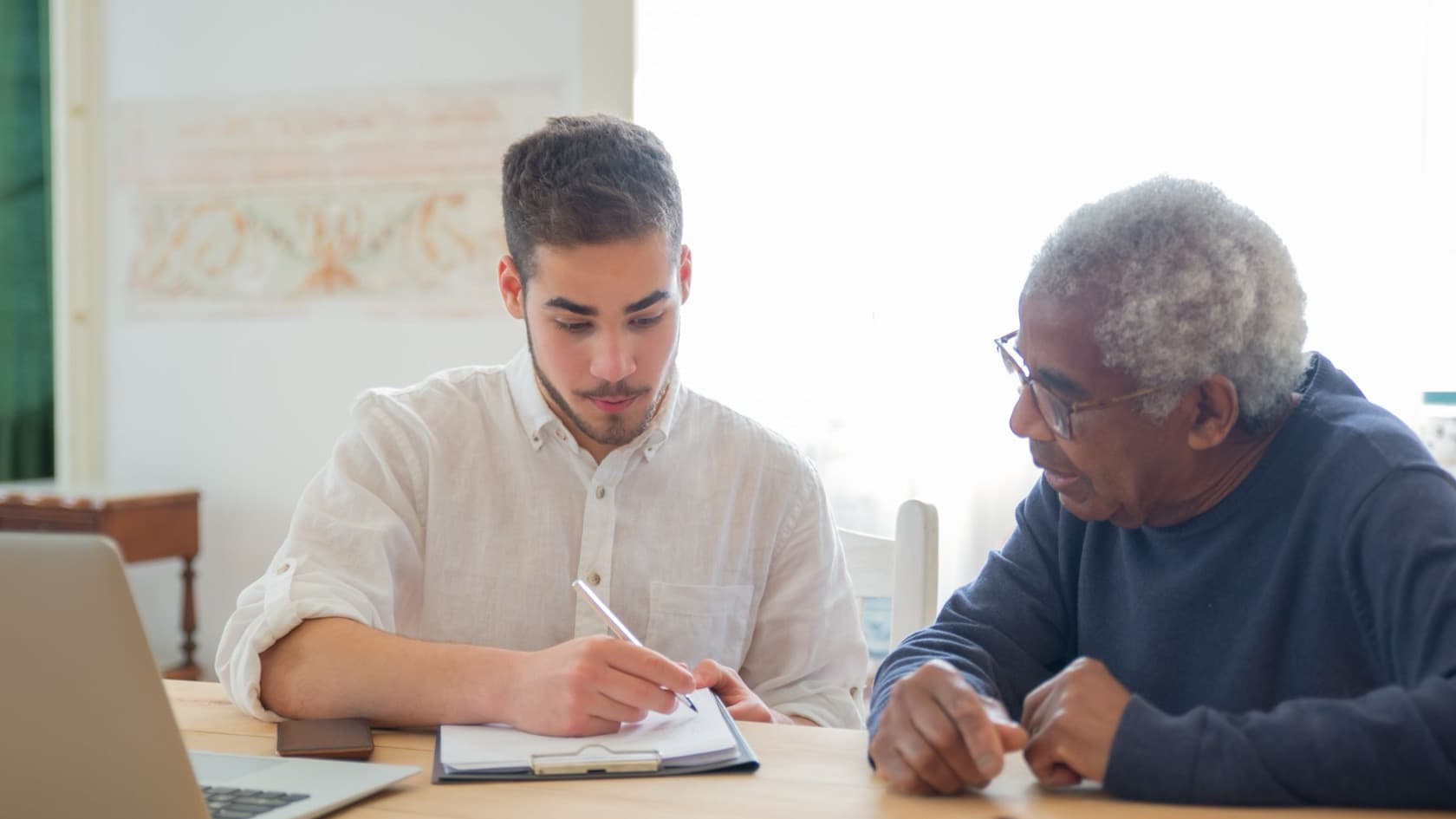 Staff member filling in an admission form on a clipboard while talking with an older man at a table