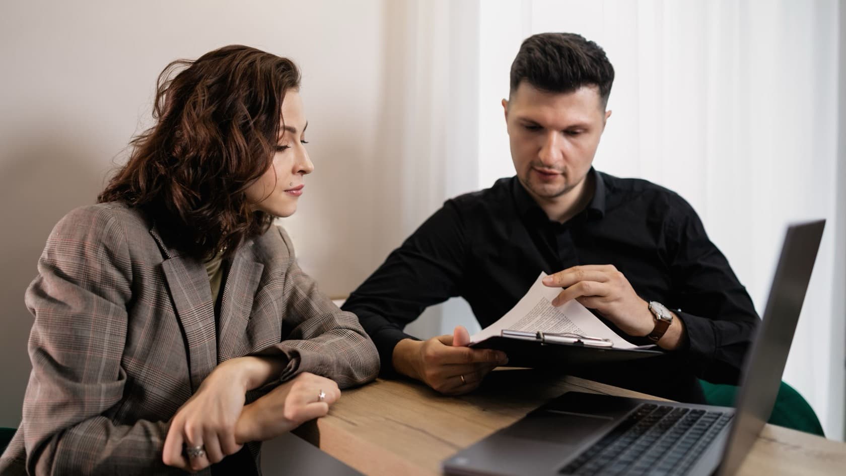 Two colleagues checking a document on a clipboard together at a desk with a laptop