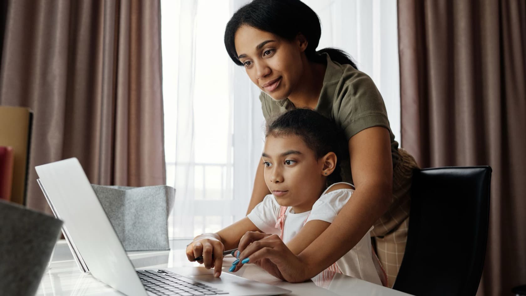 Parent and daughter looking through a website together on a laptop at home