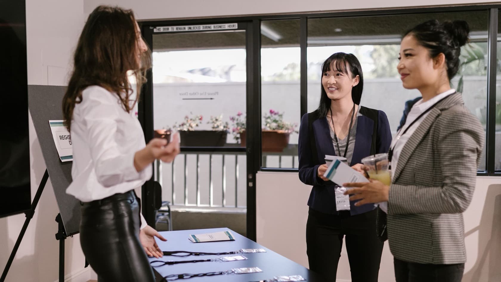 Conference guests with lanyards chatting with a host at a registration desk laid with badges