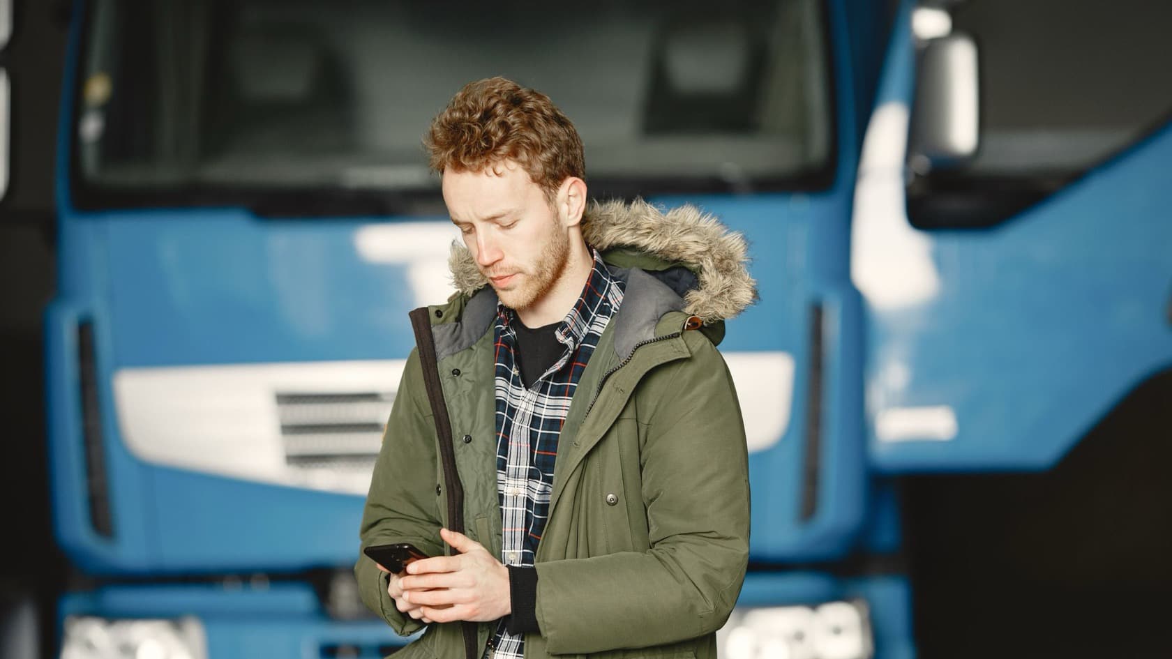 Transport coordinator checking loads on his phone in front of parked blue trucks