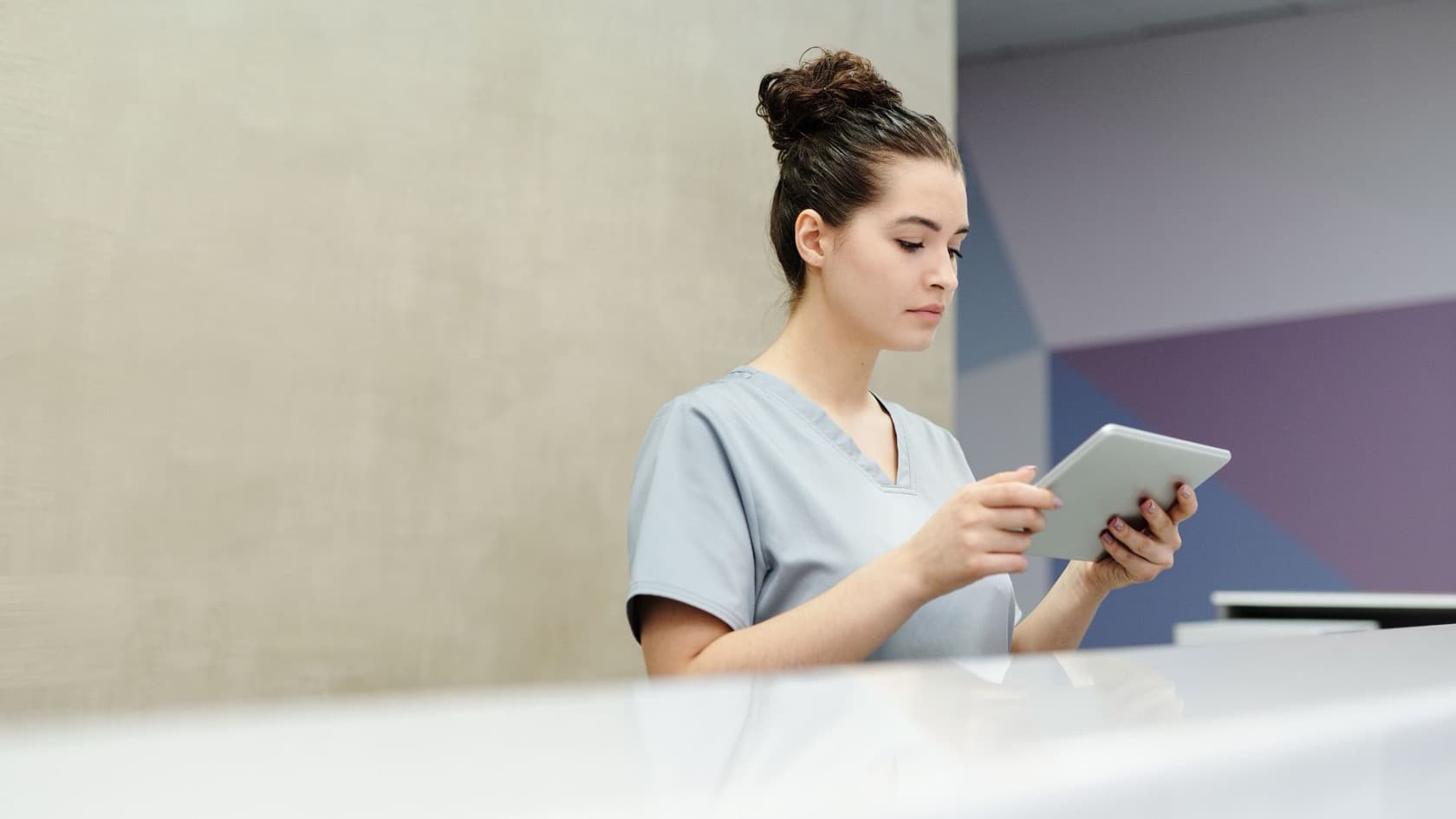 Health worker in scrubs checking details on a tablet at a reception counter