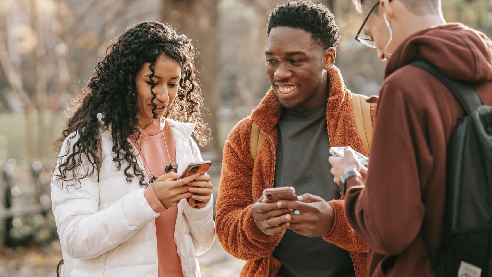 Three young people sharing something on their phones in a park