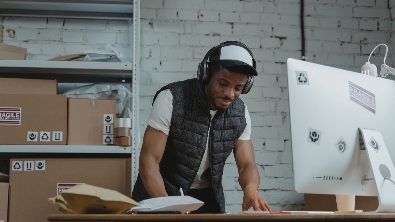 Stock clerk working at a desk computer in a stockroom lined with shelved cartons