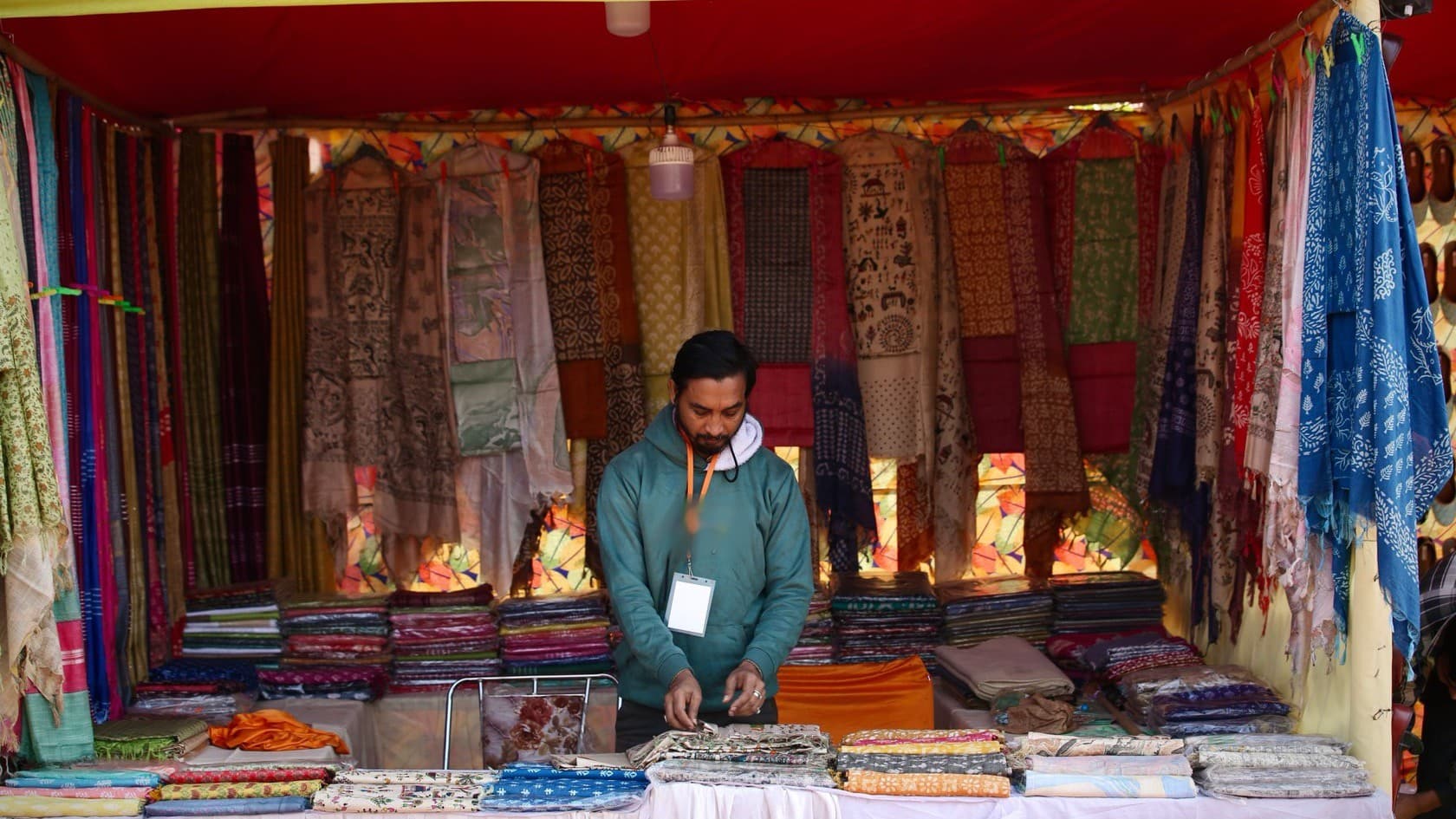 Vendor arranging hand-printed textiles at his stall at a craft fair in India