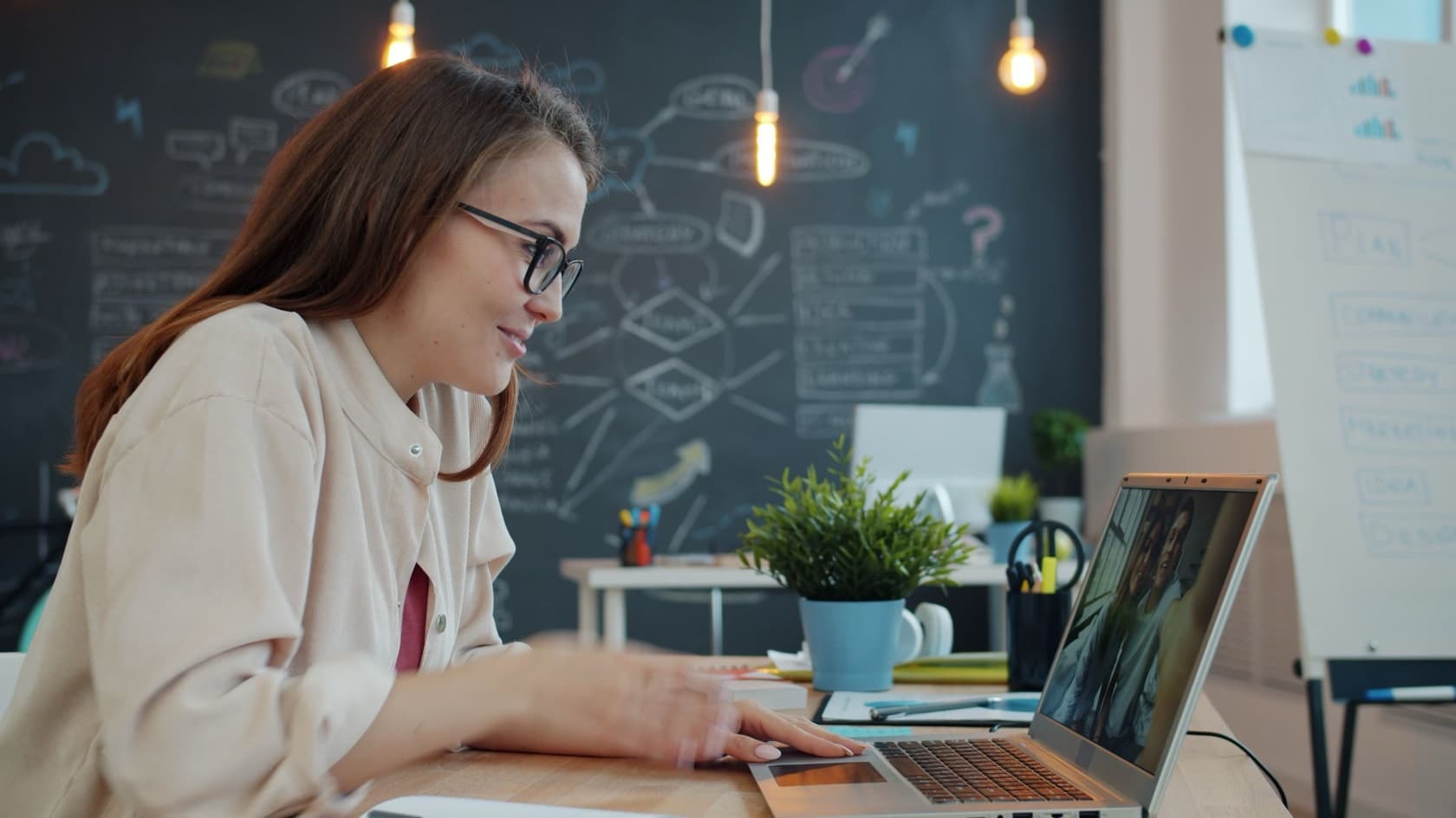 Woman joining an online session on a video call from her laptop in a bright office