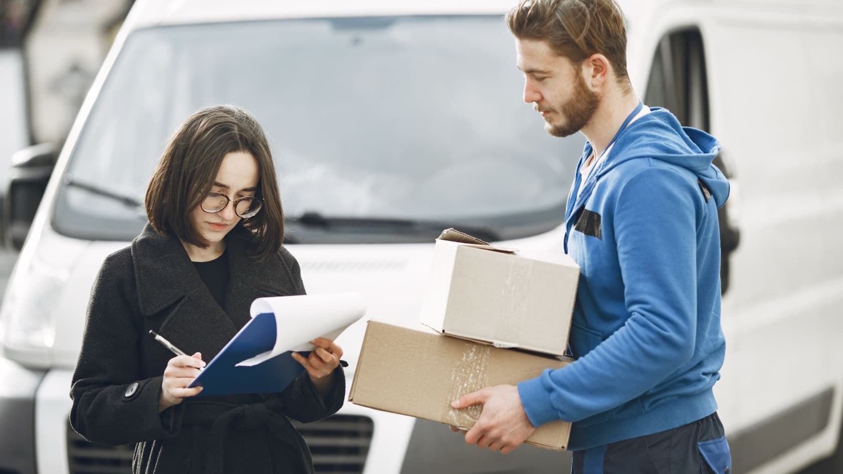 Courier handing over parcels while the customer signs for delivery beside a white van