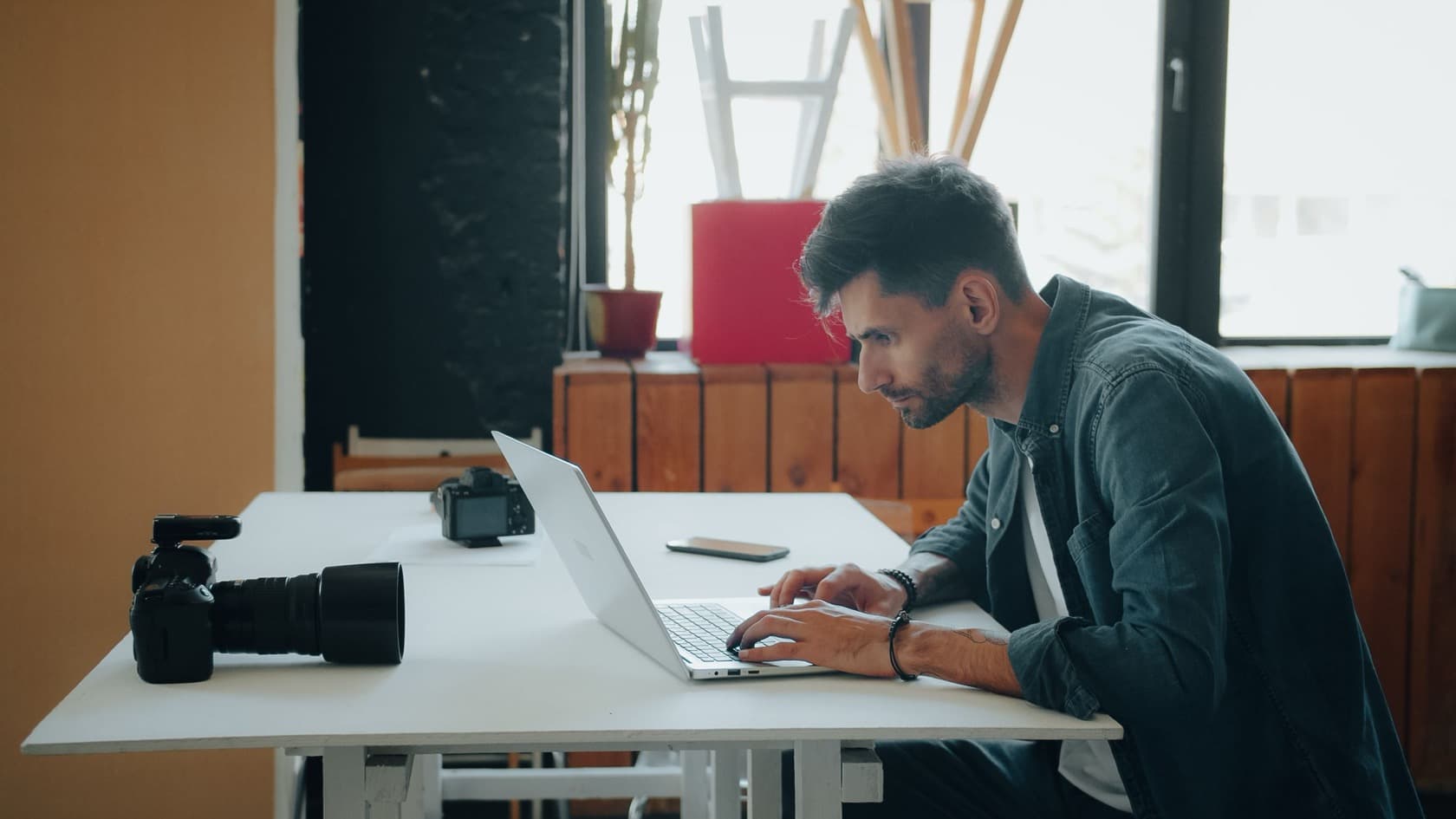 Photographer working on a laptop at a white studio desk beside two cameras
