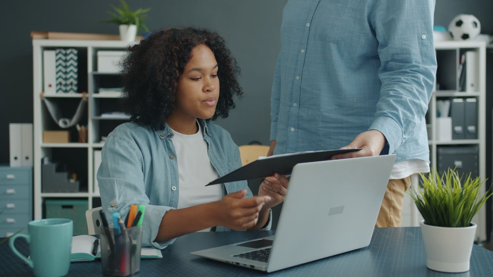 Employee at a laptop taking a document from her manager at her desk