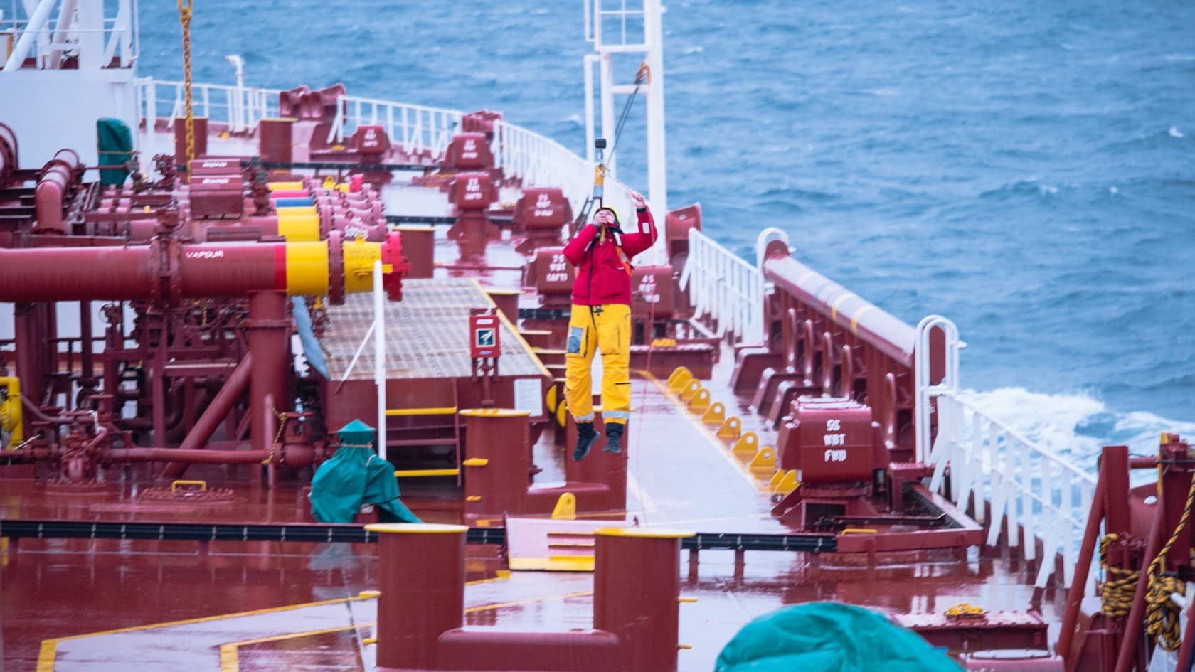 Crew member in red foul-weather gear at work on a tanker deck at sea