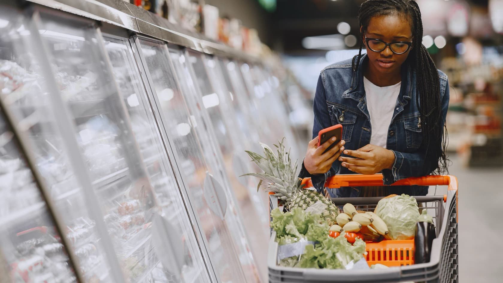 Shopper using a red phone over a cart of groceries in a supermarket aisle