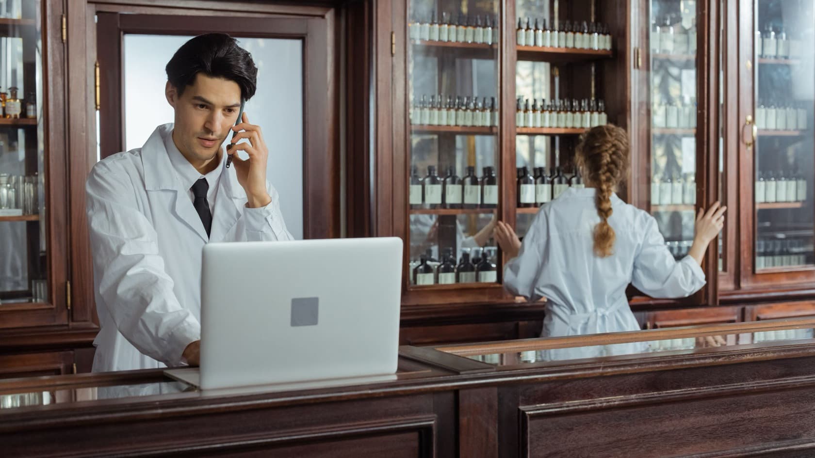Staff member taking a phone order at a laptop while a colleague checks stock