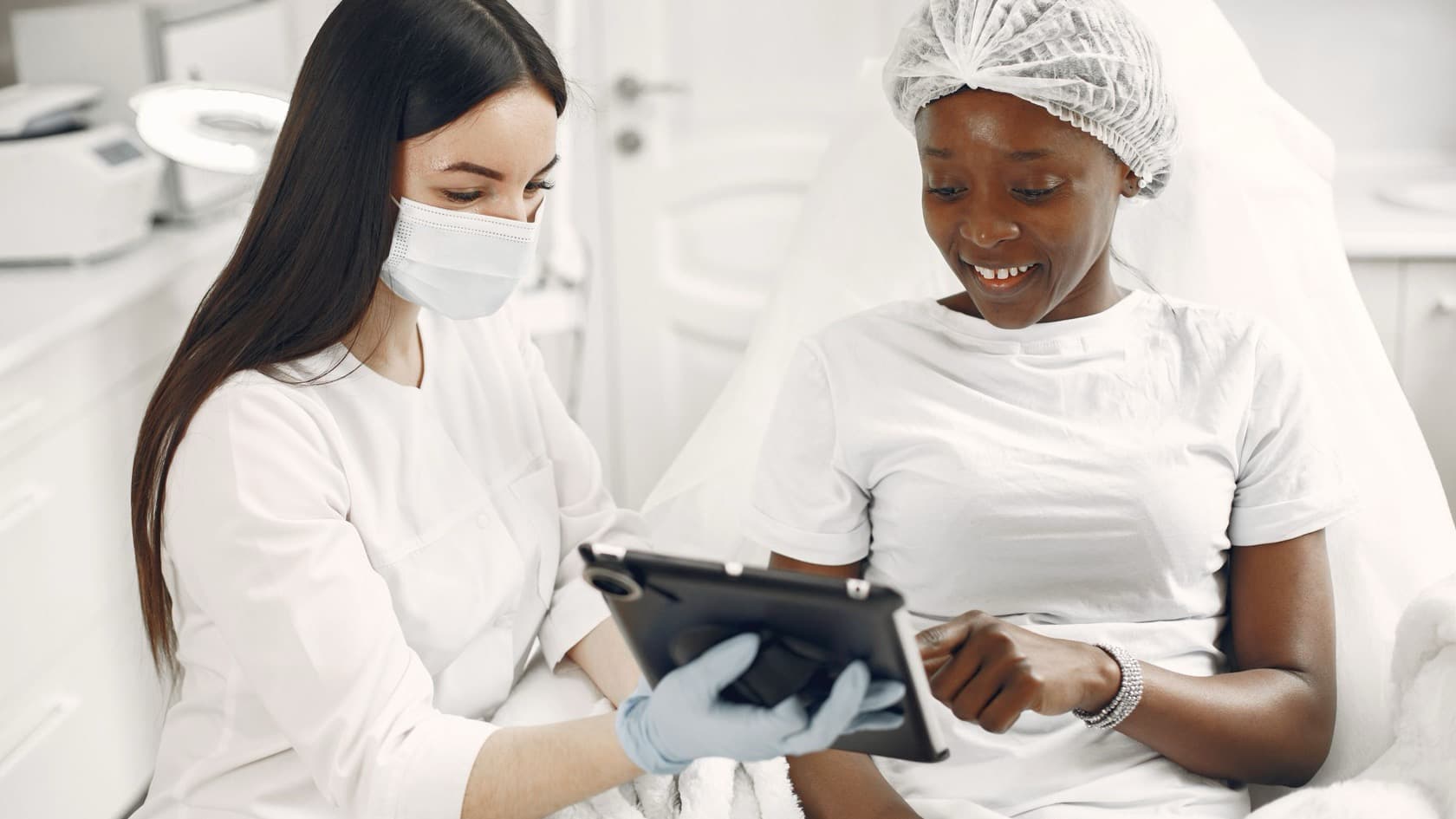 Skin clinic practitioner going through details on a tablet with a smiling patient in a treatment chair