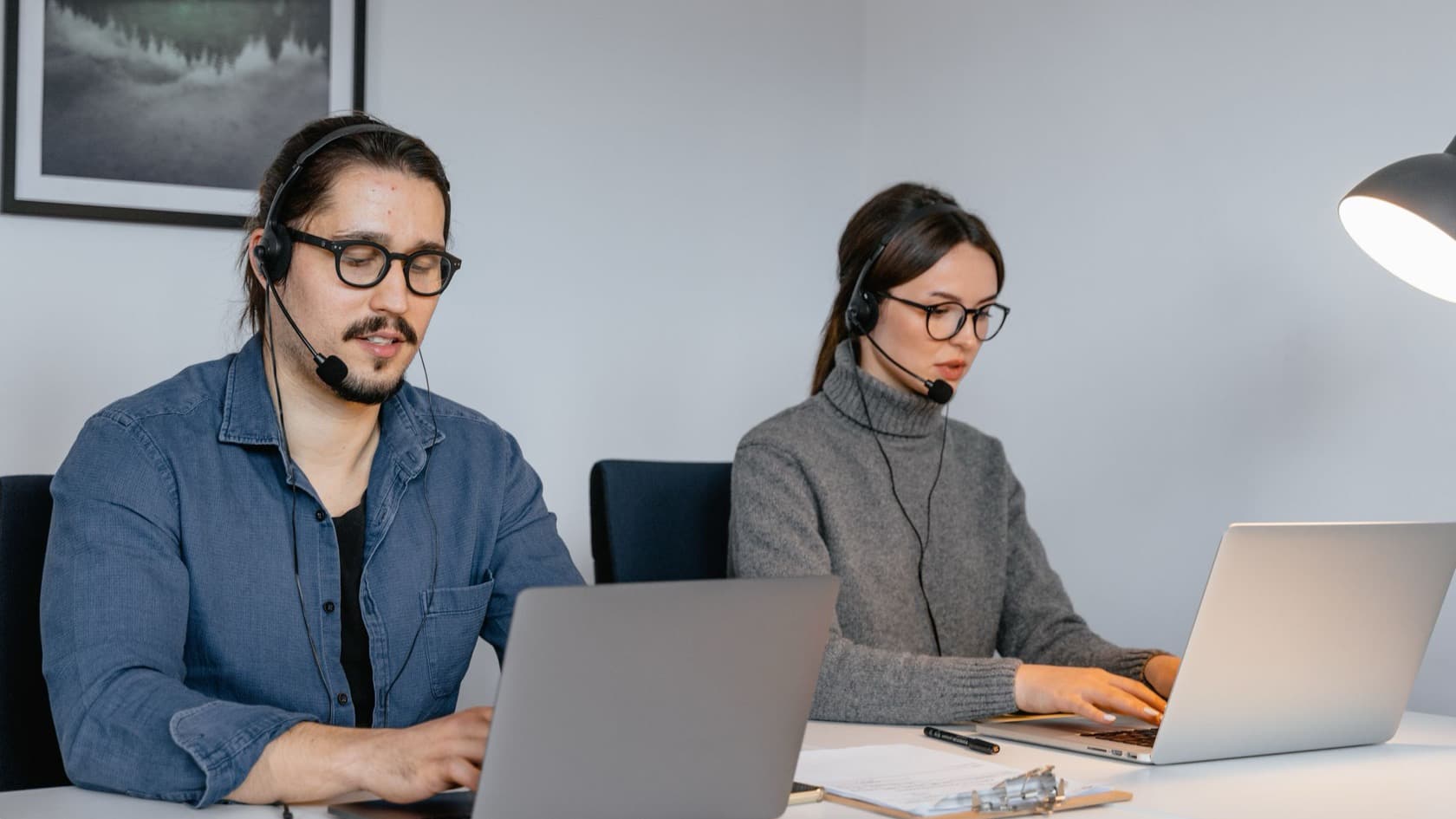 Two telecallers in headsets working through call lists on laptops at a shared desk
