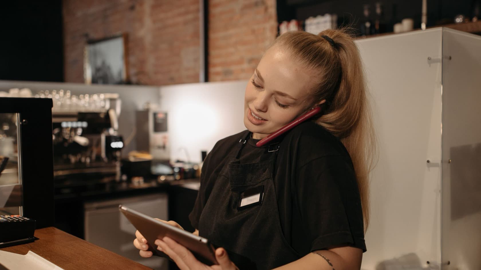 Restaurant staff member on a red phone checking a tablet at the counter