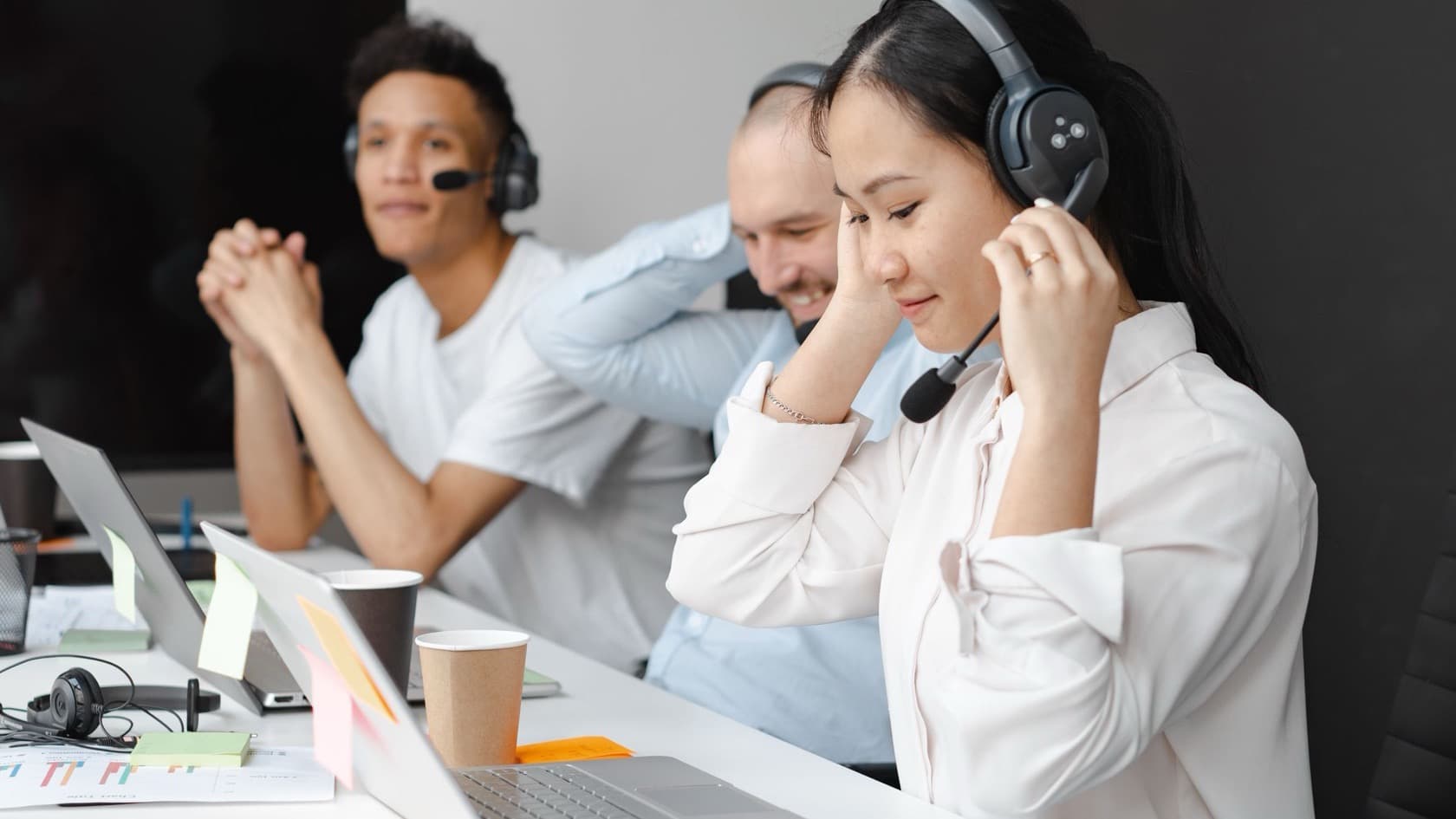 Support staff in headsets answering requests at laptops on a shared desk