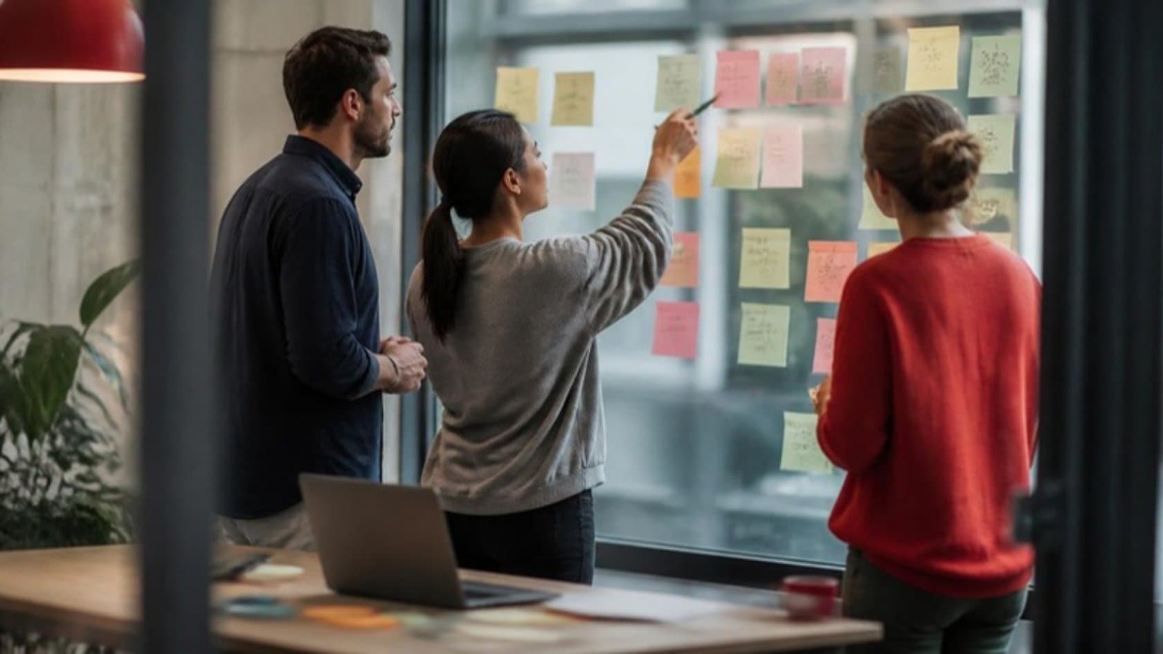 Product team sketching a SaaS minimum viable product on a glass wall covered in sticky notes