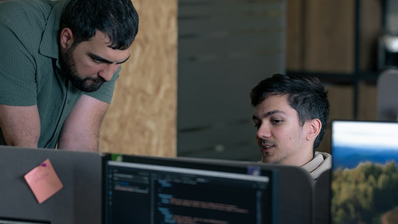 Two engineers reviewing code together on a monitor in a wood-paneled office