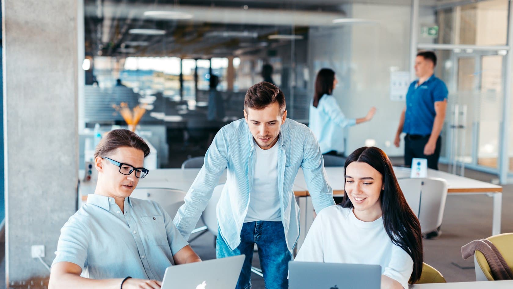 Three colleagues reviewing work together on laptops in a bright open office