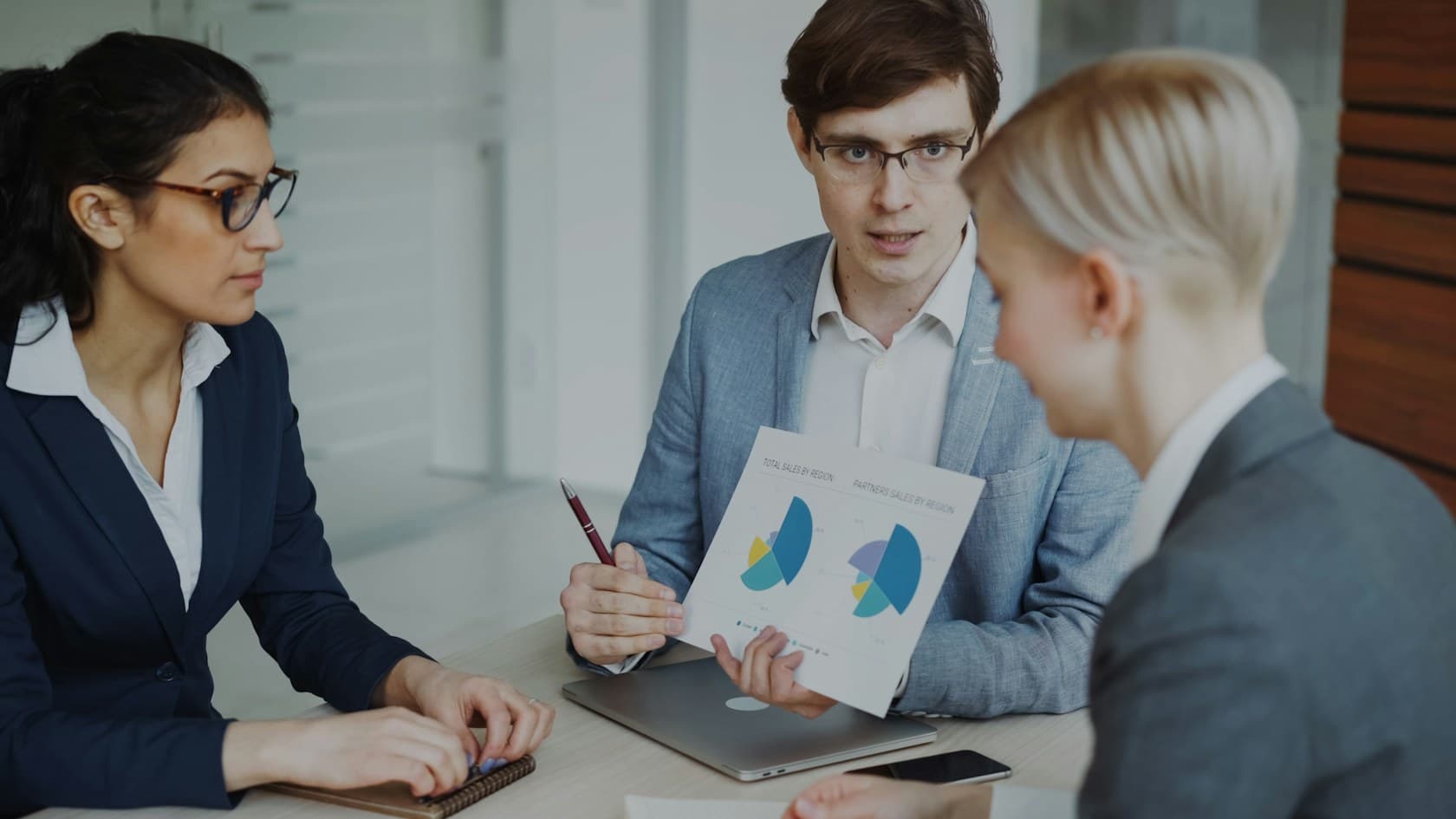 Three professionals discussing printed charts around a laptop