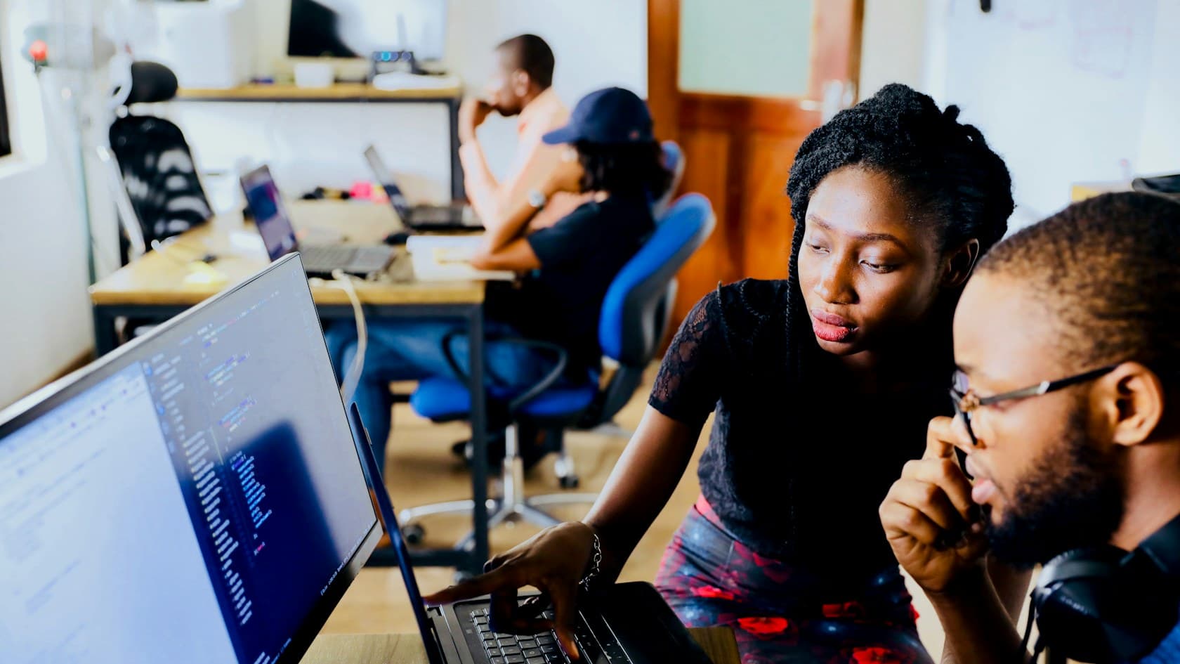Two developers reviewing code together on a laptop in a bright office