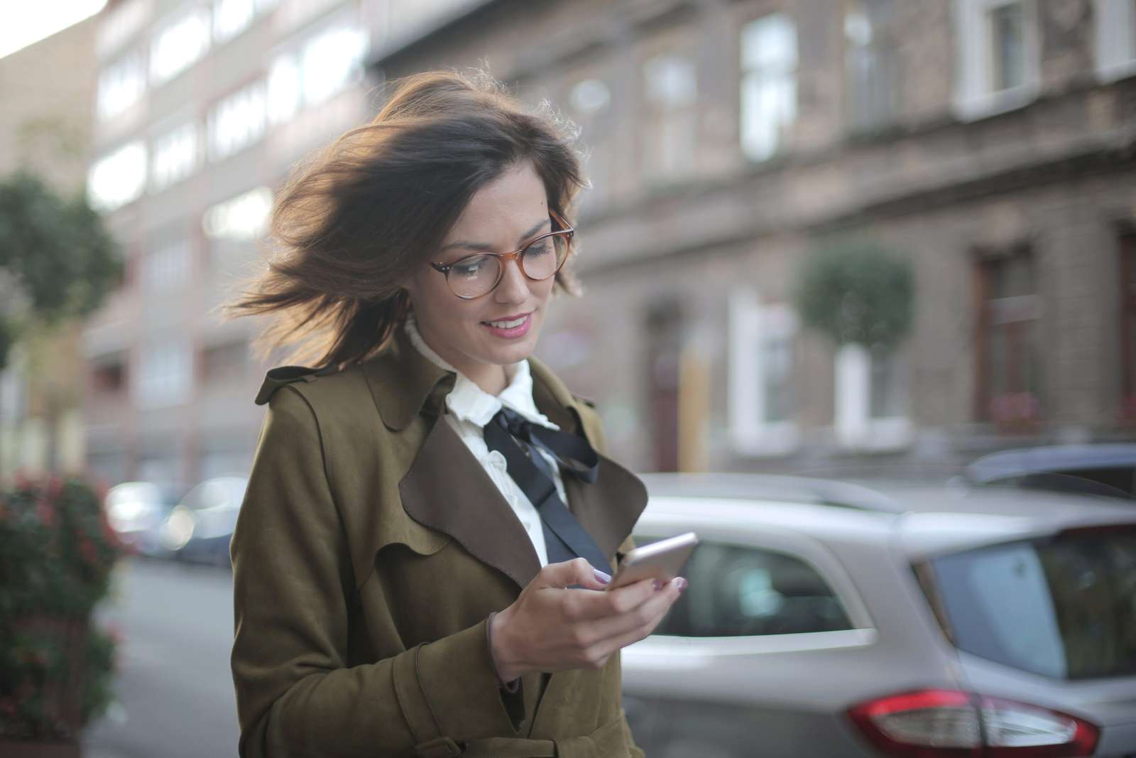 Woman in a trench coat checking her smartphone on a city street