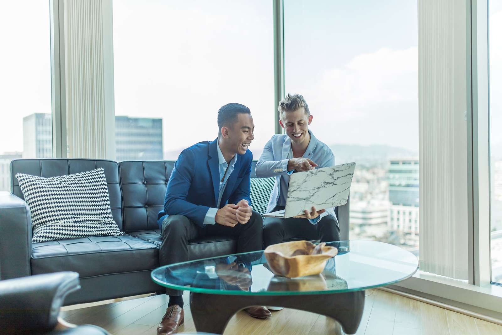 Two businessmen smiling at a laptop on an office sofa