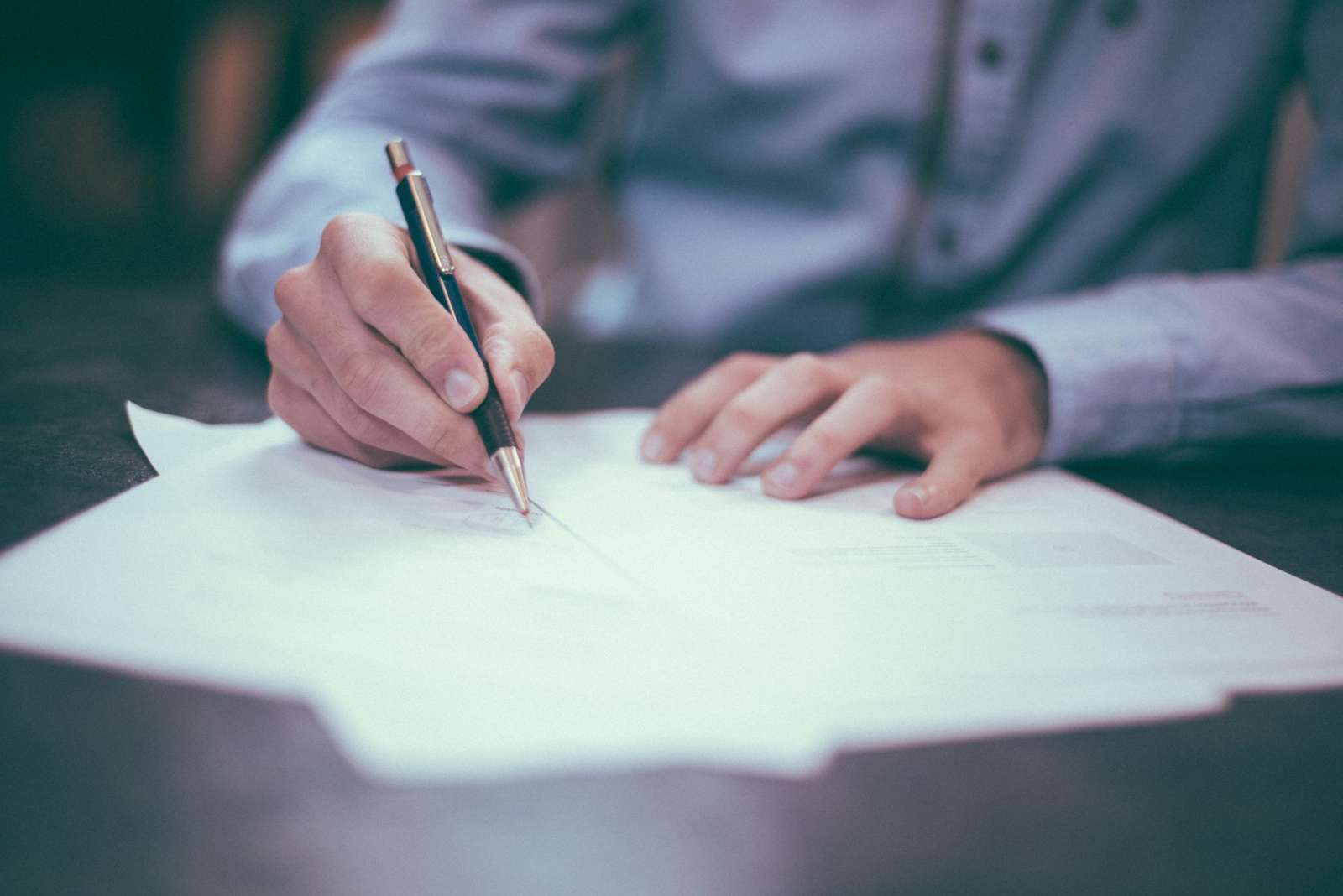 Close-up of a person signing a paper document at a desk