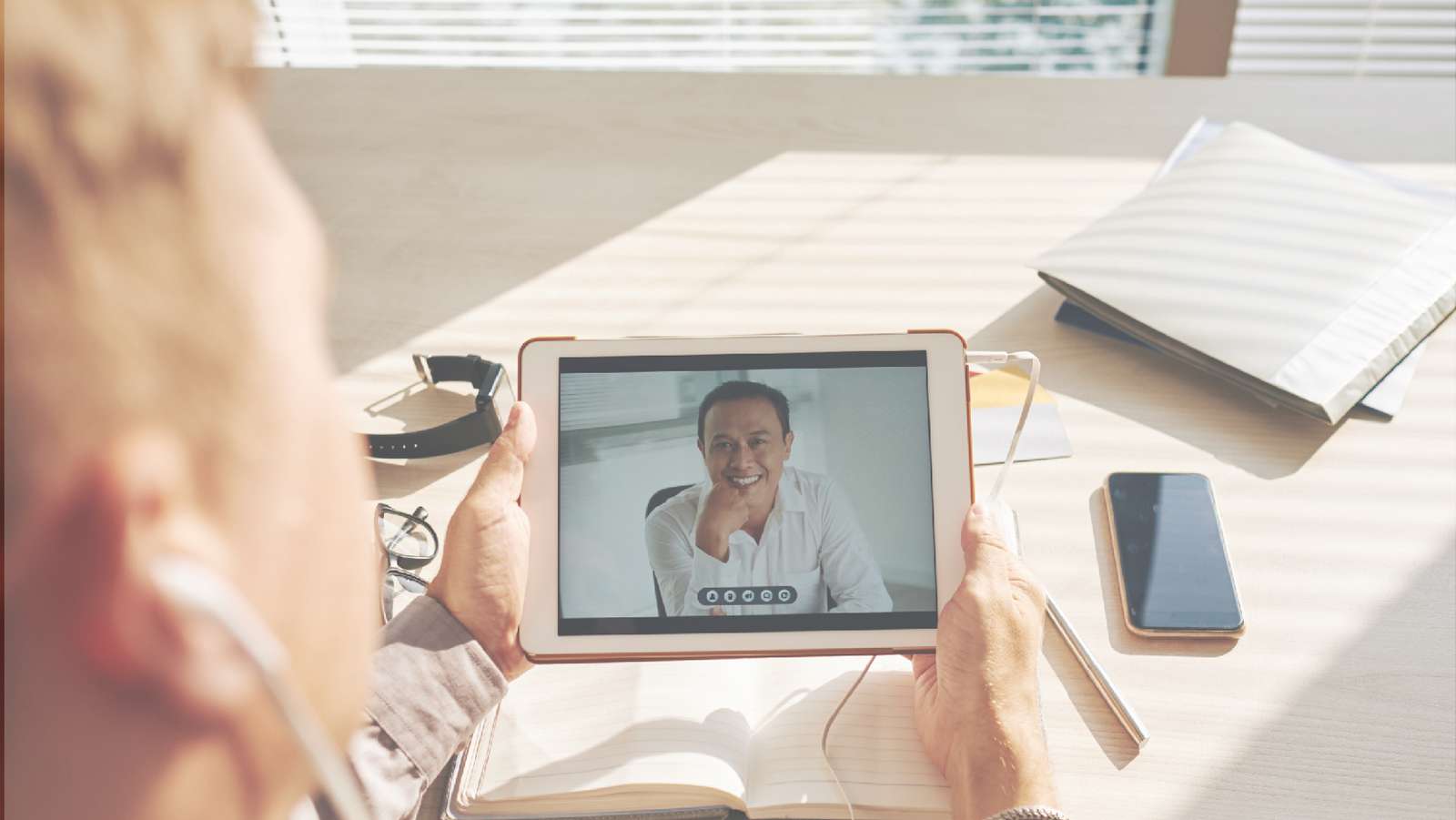 Person on a video call with a smiling colleague on a tablet at a sunlit desk